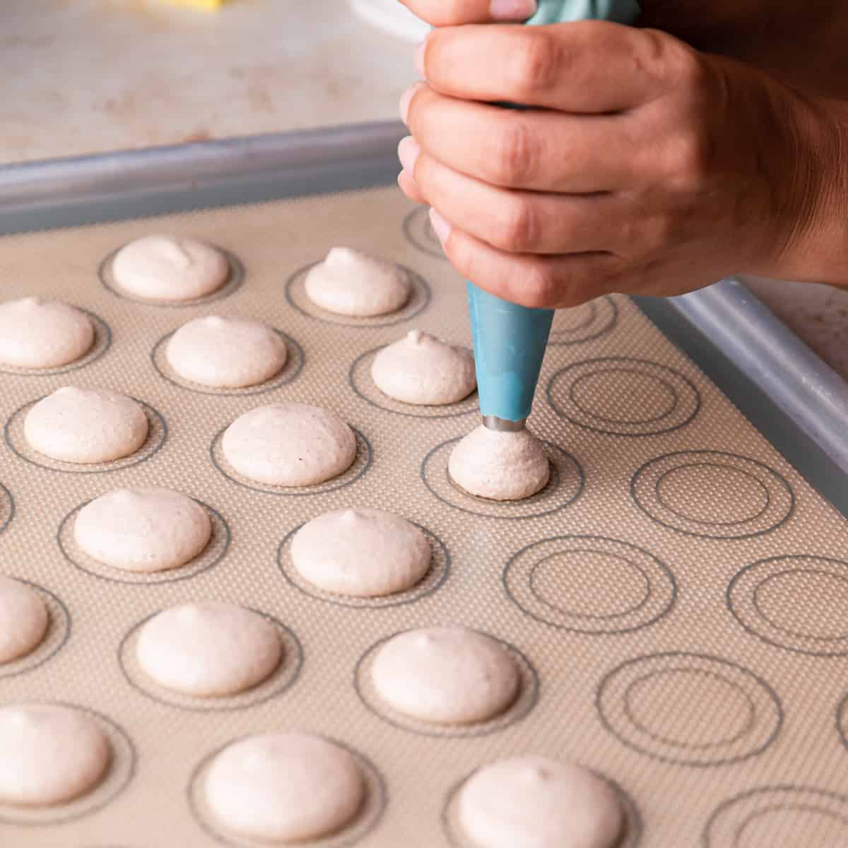 macarons being piped onto silicone mat with circles printed on it.