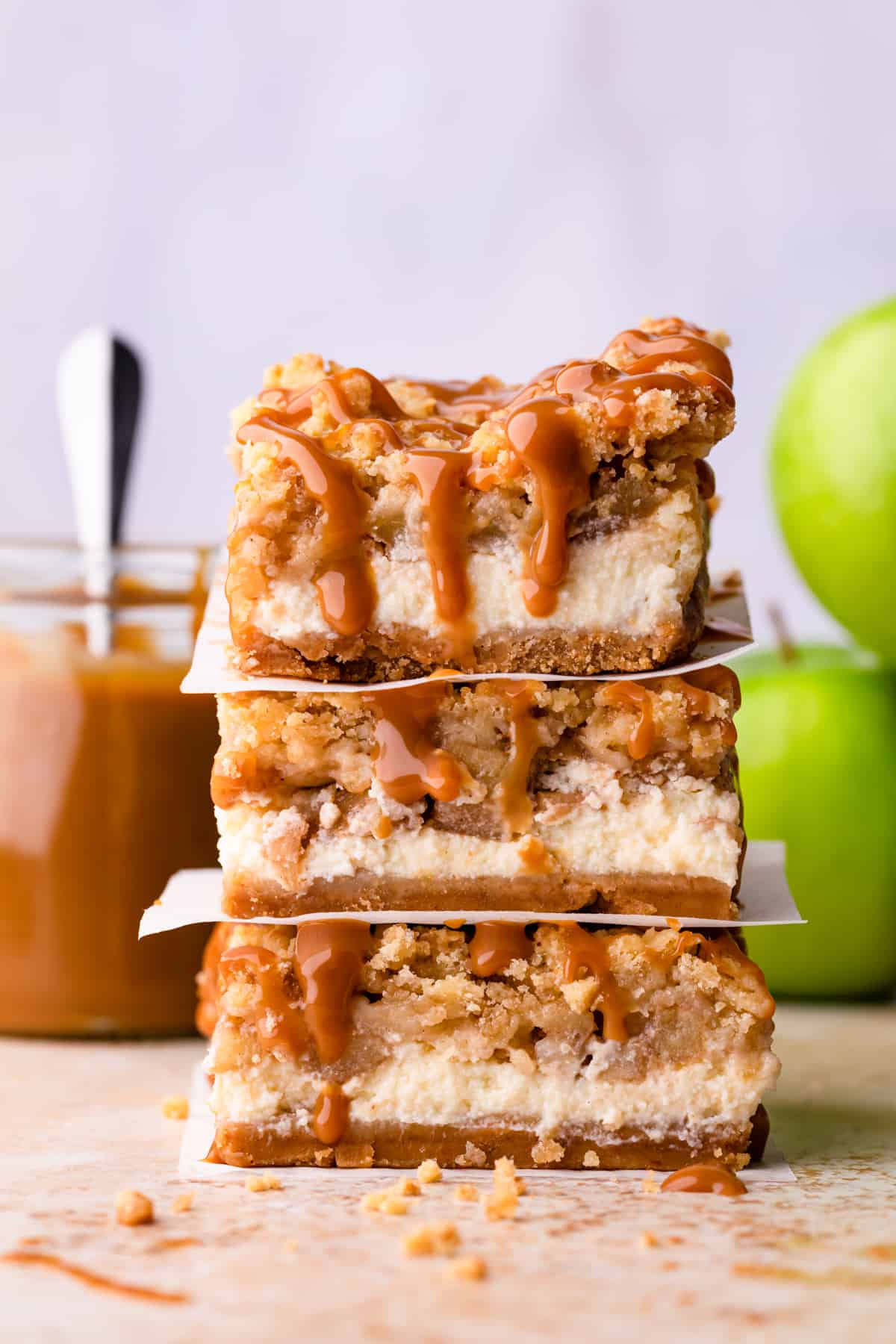 stack of three caramel apple cheesecake bars with caramel dripping from them.