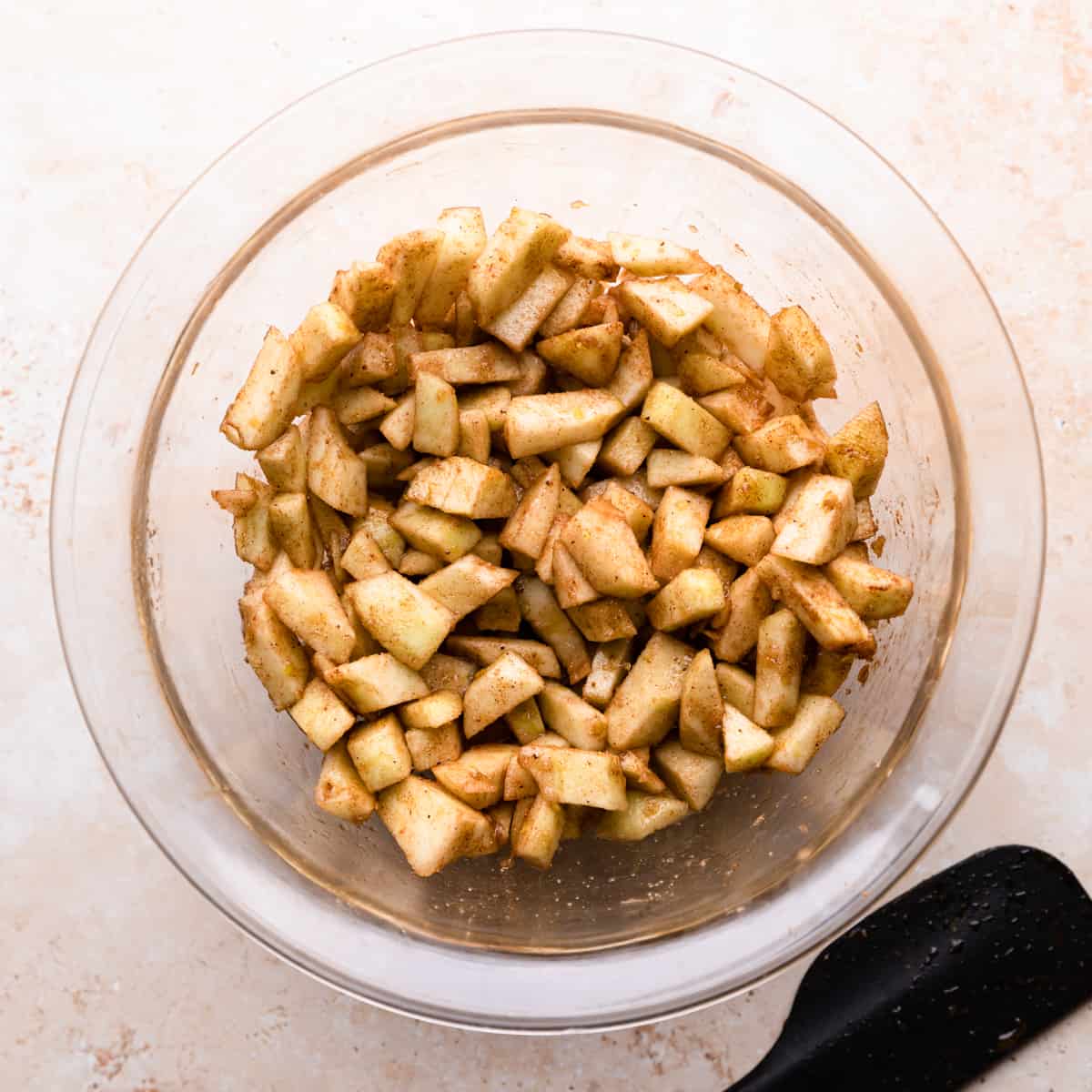 mixing bowl with chopped apples covered in spices.