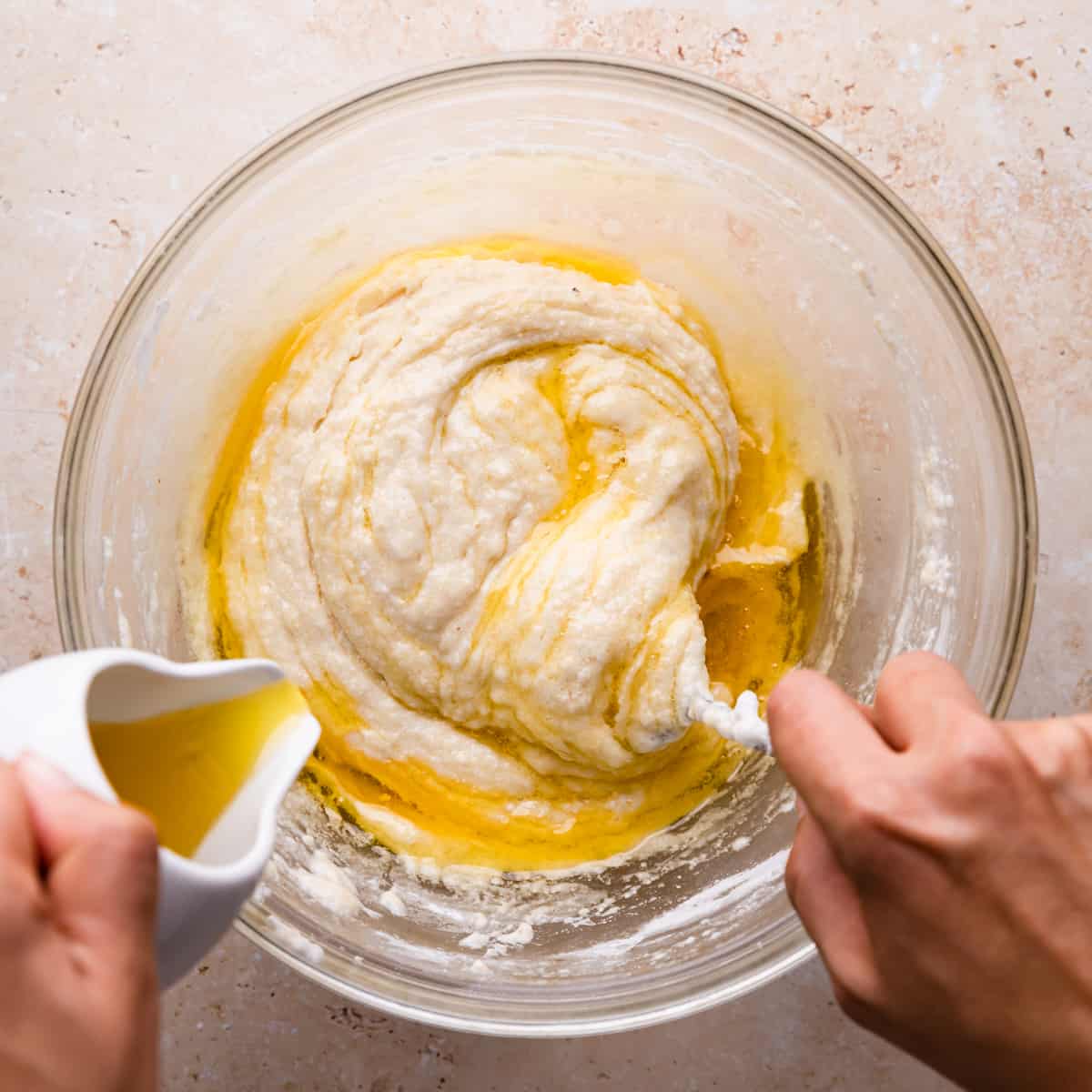 melted butter being added into cake batter in a large glass bowl.