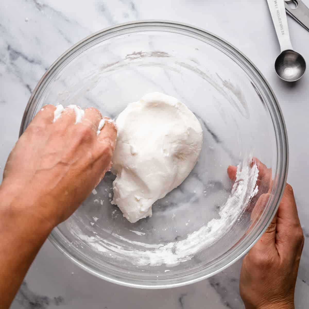 large glass bowl with white sugar paste being kneaded into dough.