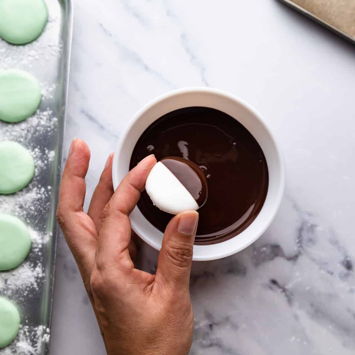 an individual mint cream being dipped in a small white bowl with melted chocolate.