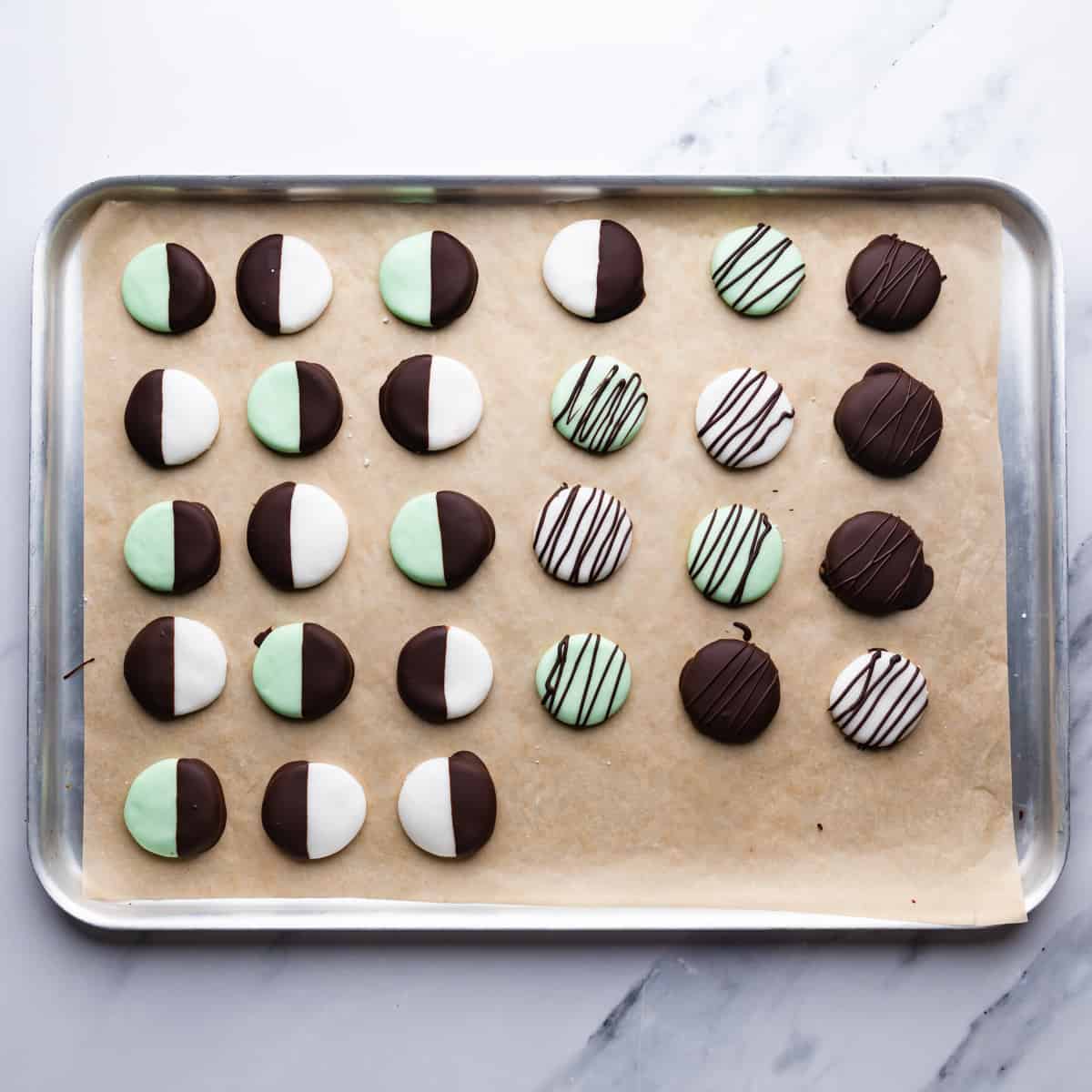 discs of mint creams dipped and drizzled with chocolate on a silver metal tray lined with brown baking paper.