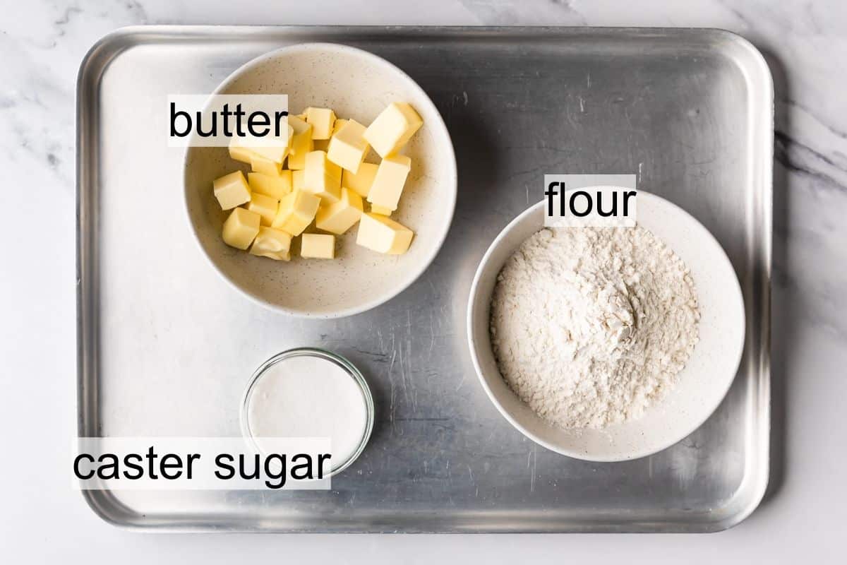 ingredients for Scottish shortbread biscuits in the bowls on a metal tray with text overlay.