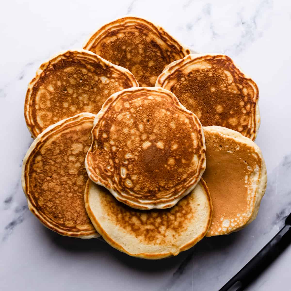 seven golden brown pancakes with small black spatula next to them.
